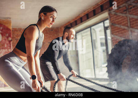 Young fitness couple in sportswear doing crossfit cardiovascular exercise using training rope at gym, healthy sports lifestyle, sport concept. Stock Photo