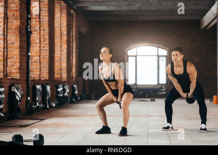 couple performing cross fit exercise. full length photo. copy space. ballistic training. power lifting .athletes doing kettlebell swing indoors Stock Photo