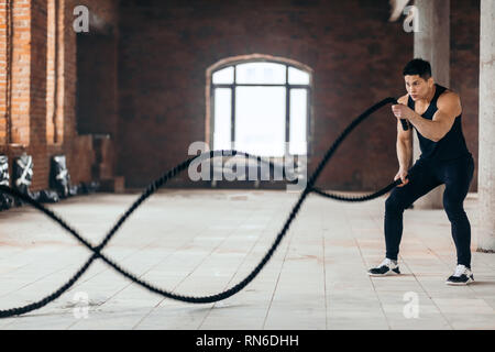 powerful guy using ropes during cross fit workout. free time. spare time, full length side view photo. copy space Stock Photo