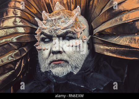 Man with thorns or warts, face covered with glitters. Demon with golden collar on black background. Alien, demon, sorcerer makeup. Fantasy concept Stock Photo