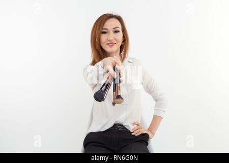 Makeup artist, beauty and people concept - Beautiful korean young woman holding make-up brushes on white background Stock Photo