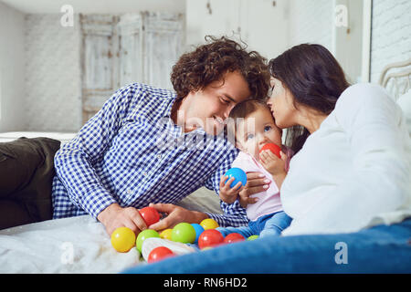 Couple kissing baby with love sitting on bed Stock Photo
