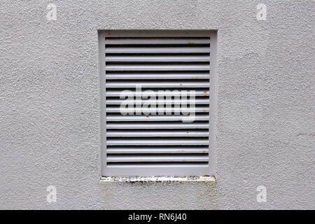 Grey metal protection bars on large industrial fan exit with partially rusted parts mounted on light grey wall on side of building on warm sunny day Stock Photo