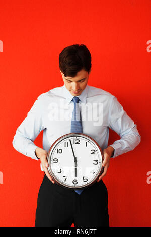 Business man holding wall clock on red background. Race against time, time goes by, running out of time, no time for work, time running, time is money Stock Photo