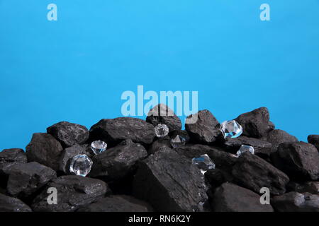 Black coal is strewn on a prism on a blue background and among it there are polished diamonds. Stock Photo