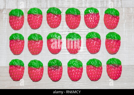 three lines of candy strawberries on a light wooden background. Stock Photo