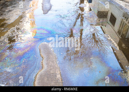 puddle from melting snow with rainbow streaks from spilled engine oil on road in city in spring day Stock Photo