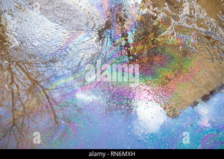 rainbow spots from spilled engine oil in puddle from melting snow on road in city in spring day Stock Photo