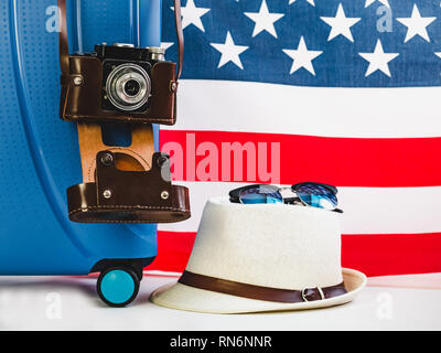 Stylish, blue suitcase, USA flag, vintage camera in a leather case on a white background, isolated. Close-up. Preparing for the summer trip Stock Photo