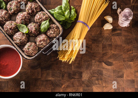 Raw feef meat balls basil tomato sauce garlic and spaghetti on butcher board. Stock Photo