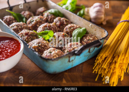 Raw feef meat balls basil tomato sauce garlic and spaghetti on butcher board. Stock Photo