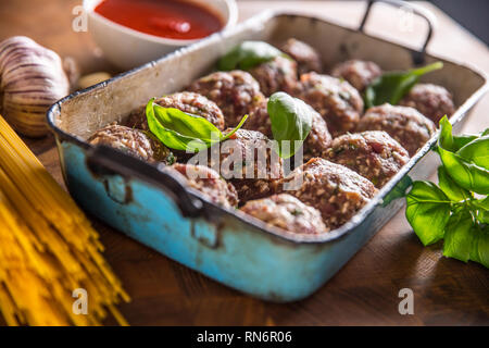 Raw feef meat balls basil tomato sauce garlic and spaghetti on butcher board. Stock Photo