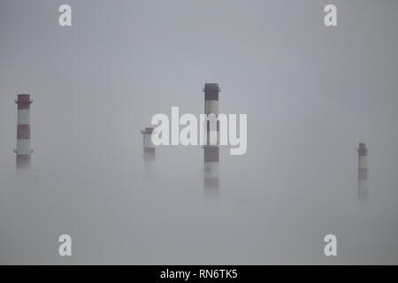 Oil refinery chimneys semi losted in the fog Stock Photo