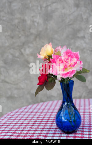 Beautiful red and pink roses in blue vase on red and white checkered table background,still life Stock Photo