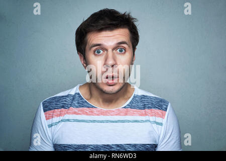 Young man with surprise emotion on gray wall background. Portrait of man with opened mouth looking at camera Stock Photo