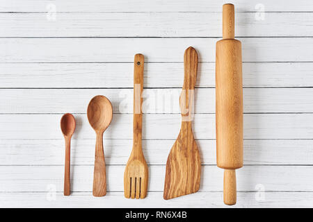 Wooden kitchen utensils on white wooden background with copy space. Spatula, spoons and rolling pin in row, top view Stock Photo