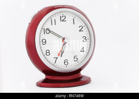 Red analogue alarm clock with luminous hands showing time at ten minutes to seven just before the alarm goes off in a morning. Perfect timing concept Stock Photo