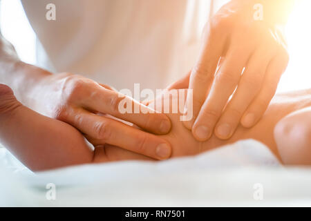 Masseur does foot massage to small child, lying on stomach on table. Stock Photo