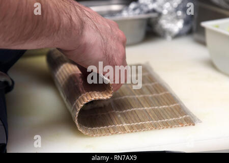 Close-up of a cook preparing sushi rolls in the kitchen of a restaurant, wrapped in a bamboo mat. The concept of cooking Japanese dishes Stock Photo