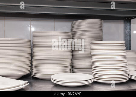 Pile of white clean ceramic porcelain plates on a metal rack in the back of the restaurant. Concept of preparation for a banquet, catering, buffet Stock Photo