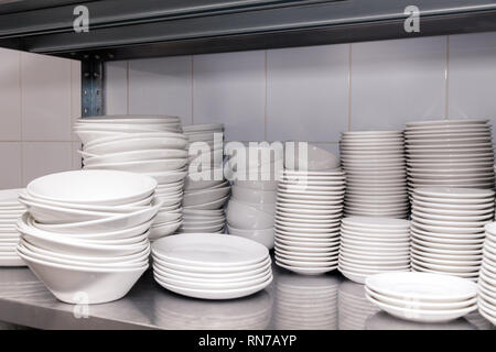 Pile of white clean ceramic porcelain plates on a metal rack in the back of the restaurant. Concept of preparation for a banquet, catering, buffet Stock Photo
