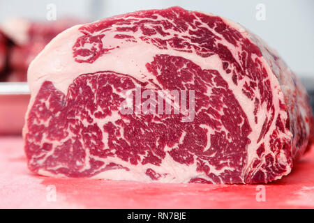 Closeup macro pieces ribeye marbled beef steak on red plastic cutting board on metal table in restaurant kitchen. Concept packing semi-finished produc Stock Photo