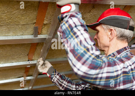 Drywall plaster wall metal fixation. Man holding metal ruler against metal frame on unfinished attic ceiling Stock Photo