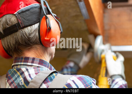 Man fixing metal frame using angle grinder on attic ceiling covered with rock wool Stock Photo