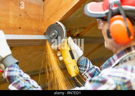 Man fixing metal frame using angle grinder on attic ceiling covered with rock wool Stock Photo