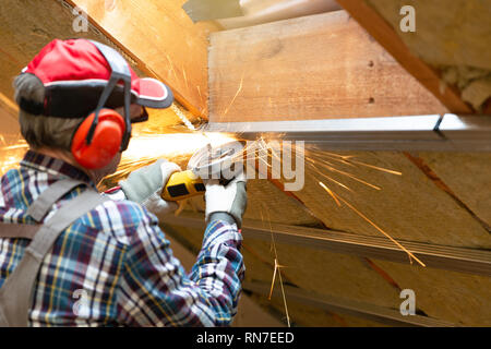 Man fixing metal frame using angle grinder on attic ceiling covered with rock wool Stock Photo