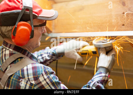 Man fixing metal frame using angle grinder on attic ceiling covered with rock wool Stock Photo