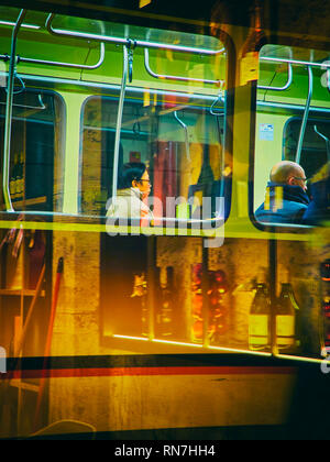 A tram transporting an Oriental men in Milan at night. Lombardy, Italy. View through the reflection of the storefront of a bar. Stock Photo