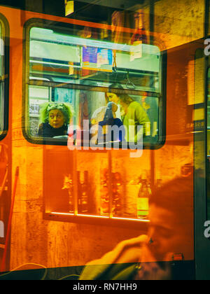 A tram transporting citizens in Milan at night. Lombardy, Italy. View through the reflection of the storefront of a bar. Stock Photo