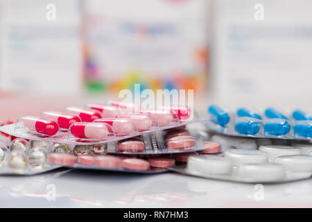 Heap of medical pills in white, blue and other colors on white mirror background. Pills in plastic package. Concept of healthcare and medicine. Stock Photo