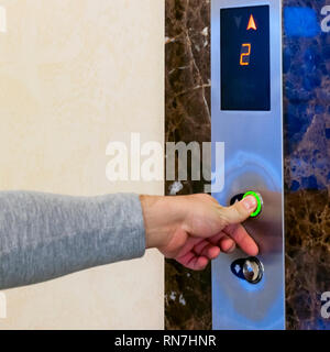 Finger presses the elevator button. Green button. Hand reaches for the button of the elevator call Stock Photo