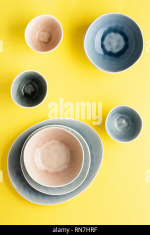 Beautiful blue, grey, beige dinnerware, plates bowls on yellow background table, top view, selective focus Stock Photo