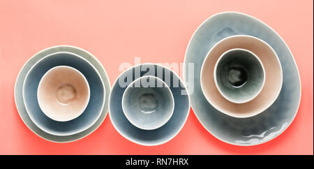 Beautiful blue, grey, beige dinnerware, plates bowls on trendy coral background table, top view, selective focus Stock Photo