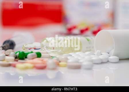 Scattered tablets, pills, ampules for injection with a syringe on white mirror background. Health care concept. Scattered supplements from plastic bot Stock Photo