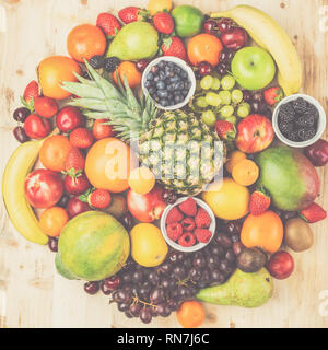 Circle filled with healthy colorful fruits, strawberries raspberries oranges plums apples kiwis grapes blueberries mango persimmon on light wooden table, top view, toned, selective focus Stock Photo