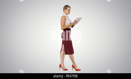 Businesswoman using electronic tab walking on gradient background. Stock Photo