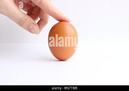 Finger holds a brown chicken egg in a vertical state isolated on a light background Stock Photo