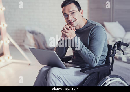 Modern device. Joyful disabled man using a laptop while resting at home Stock Photo