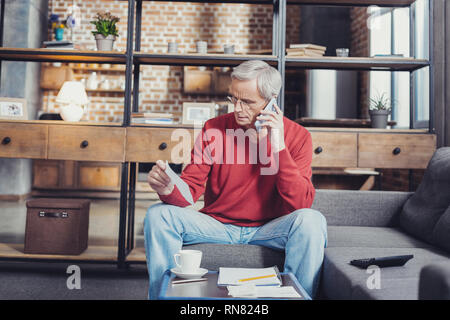 Phone talk. Calm clever aged man looking serious while having an important phone conversation with a bank worker Stock Photo