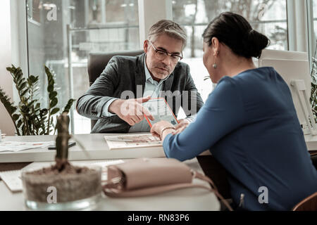 Grey-haired serious man in eyeglasses showing schemes to his colleague Stock Photo