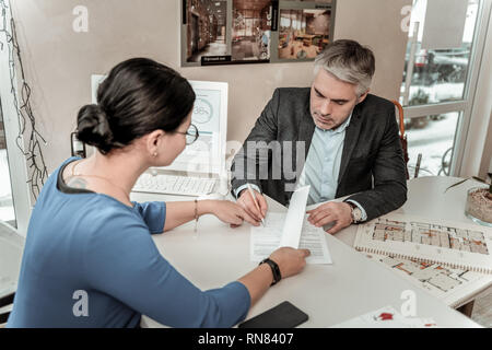 Serious grey-haired handsome man in eyeglasses putting his signature on the document Stock Photo