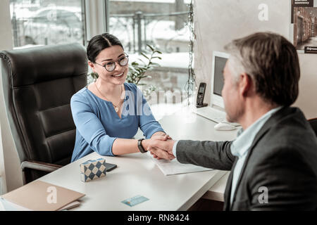 Dark-haired beautiful asian woman in a blue shirt shaking hands with a new employee Stock Photo