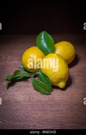 Still life of fresh lemons with their leaves on dark aged wooden background Stock Photo
