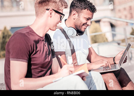 Online education. Two friends sitting in semi position and feeling happiness while completing task Stock Photo
