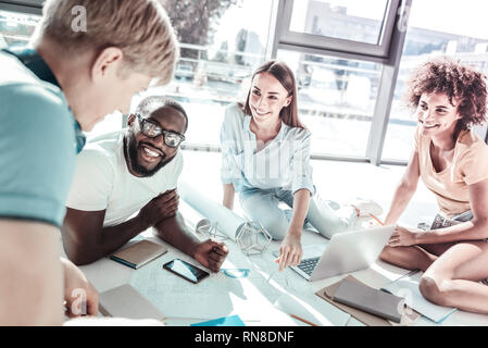 Creating plan. Pretty females sitting on the floor and listening to their partners, being in the office Stock Photo