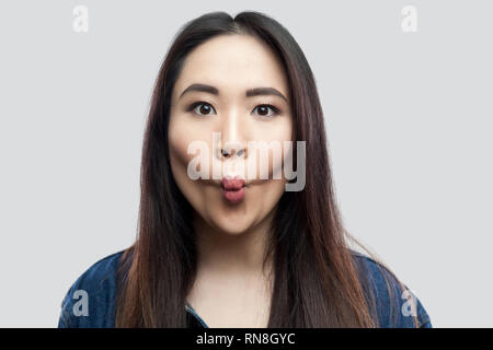 Portrait of funny beautiful brunette asian young woman in casual blue denim jacket with makeup standing with big eyes and fish lips looking. indoor st Stock Photo